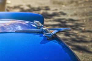 A blue 55 Chevy with a chrome emblem on the hood